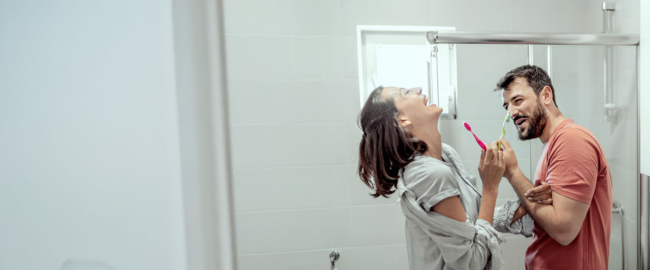 Coppia ride in bagno con spazzolini colorati in mano, pronti a lavarsi i denti.
