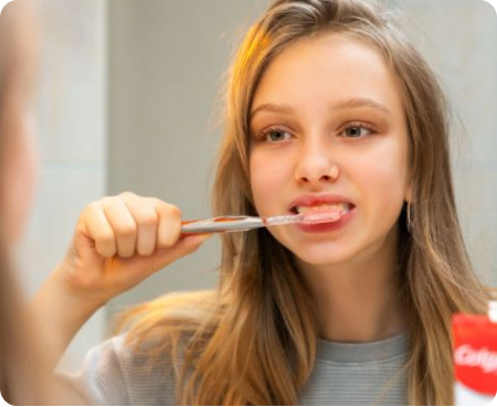 Una ragazza si lava i denti davanti allo specchio come parte di una sana routine di igiene orale.