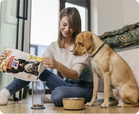 Una donna versa il cibo Hill's Pet Nutrition in un contenitore graduato mentre un cane guarda con attenzione.