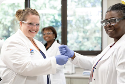 Due scienziati con camici e guanti sorridono e si stringono la mano in un laboratorio