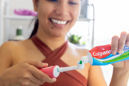 Una donna sorride mentre mette il dentifricio Colgate su uno spazzolino da denti in un bagno.